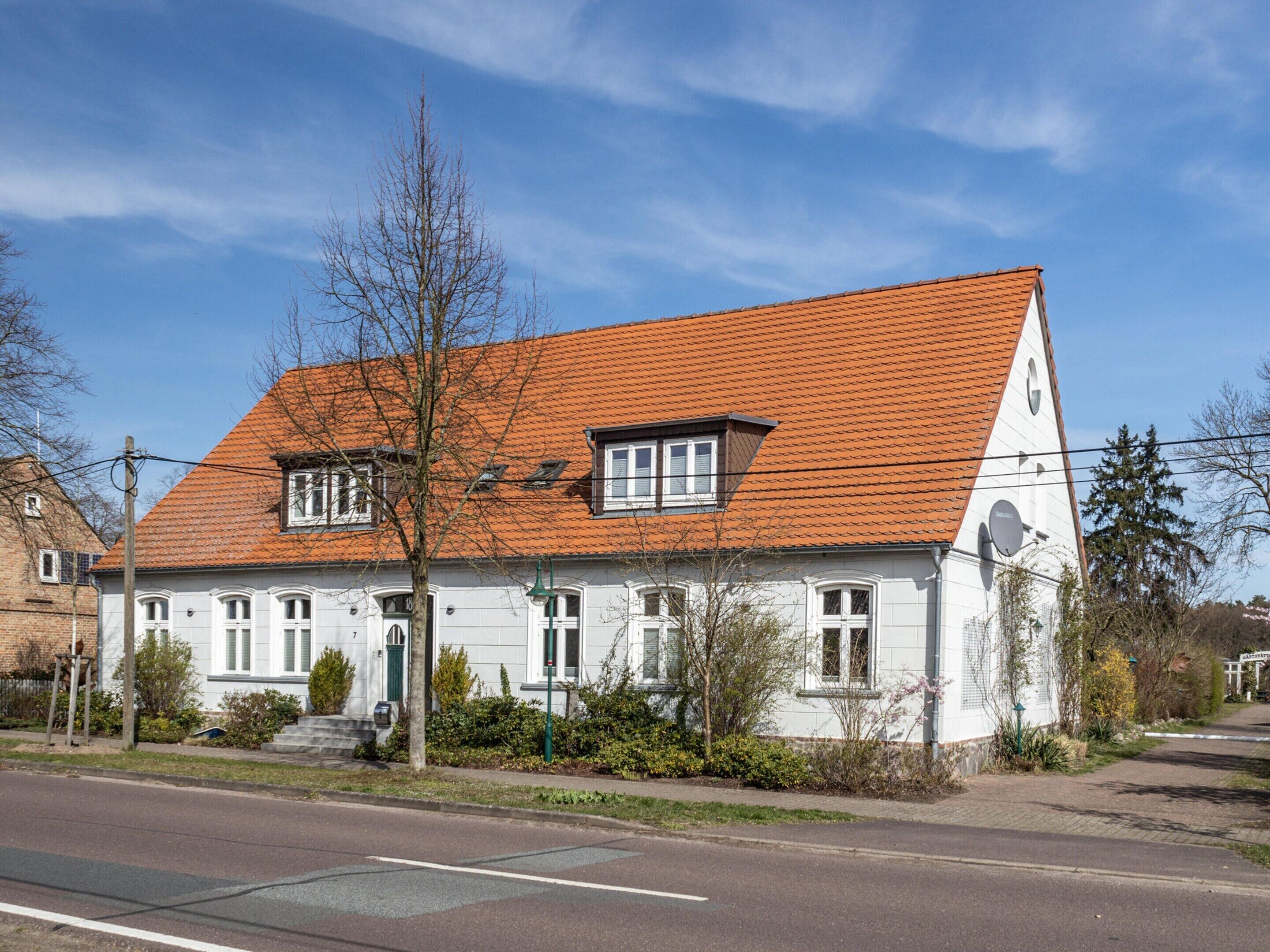 A two-story white building with a red-tiled roof, multiple windows, and a small front porch.