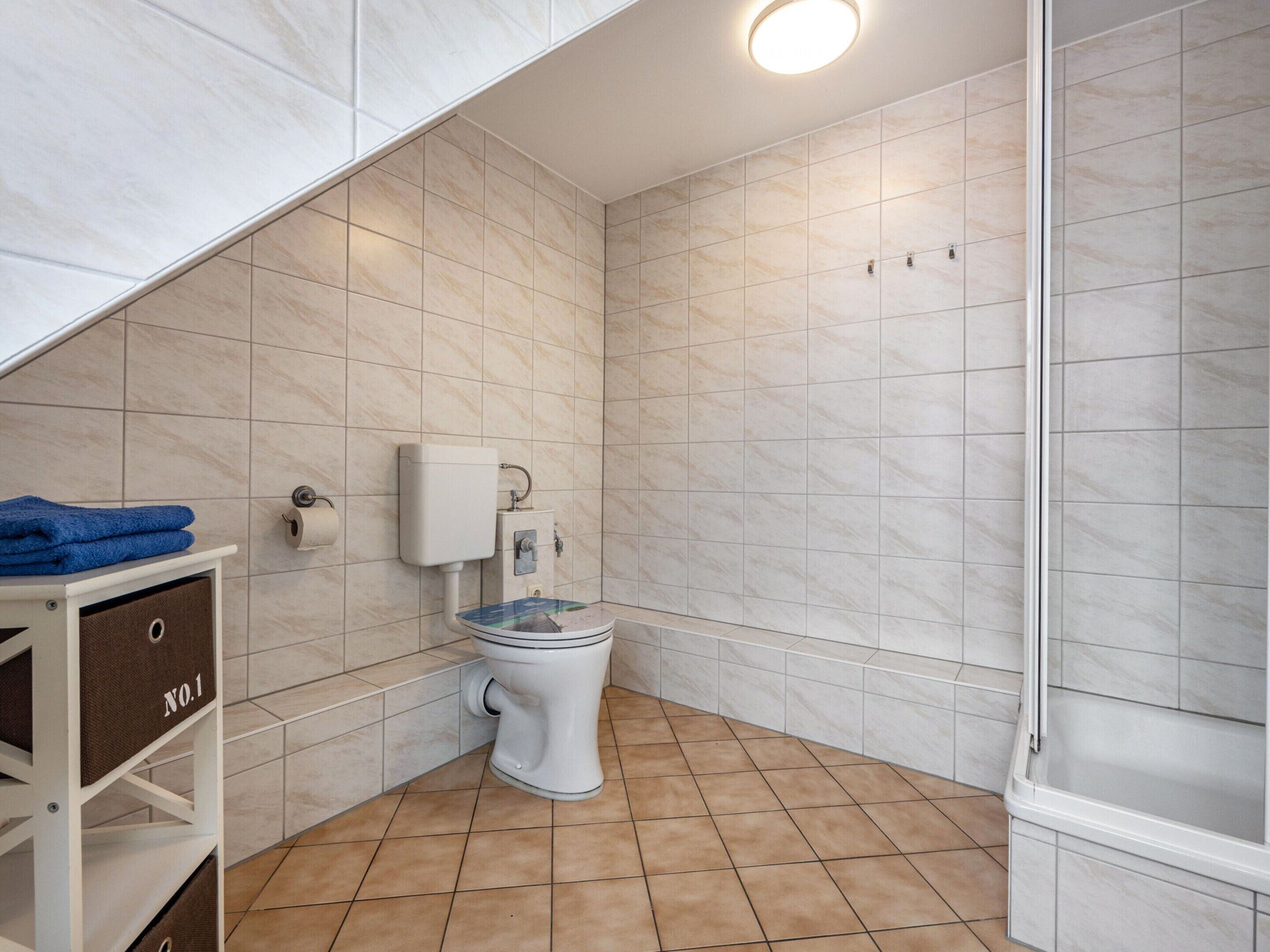 A bathroom with a toilet, a shelf with storage bins, and a shower area.