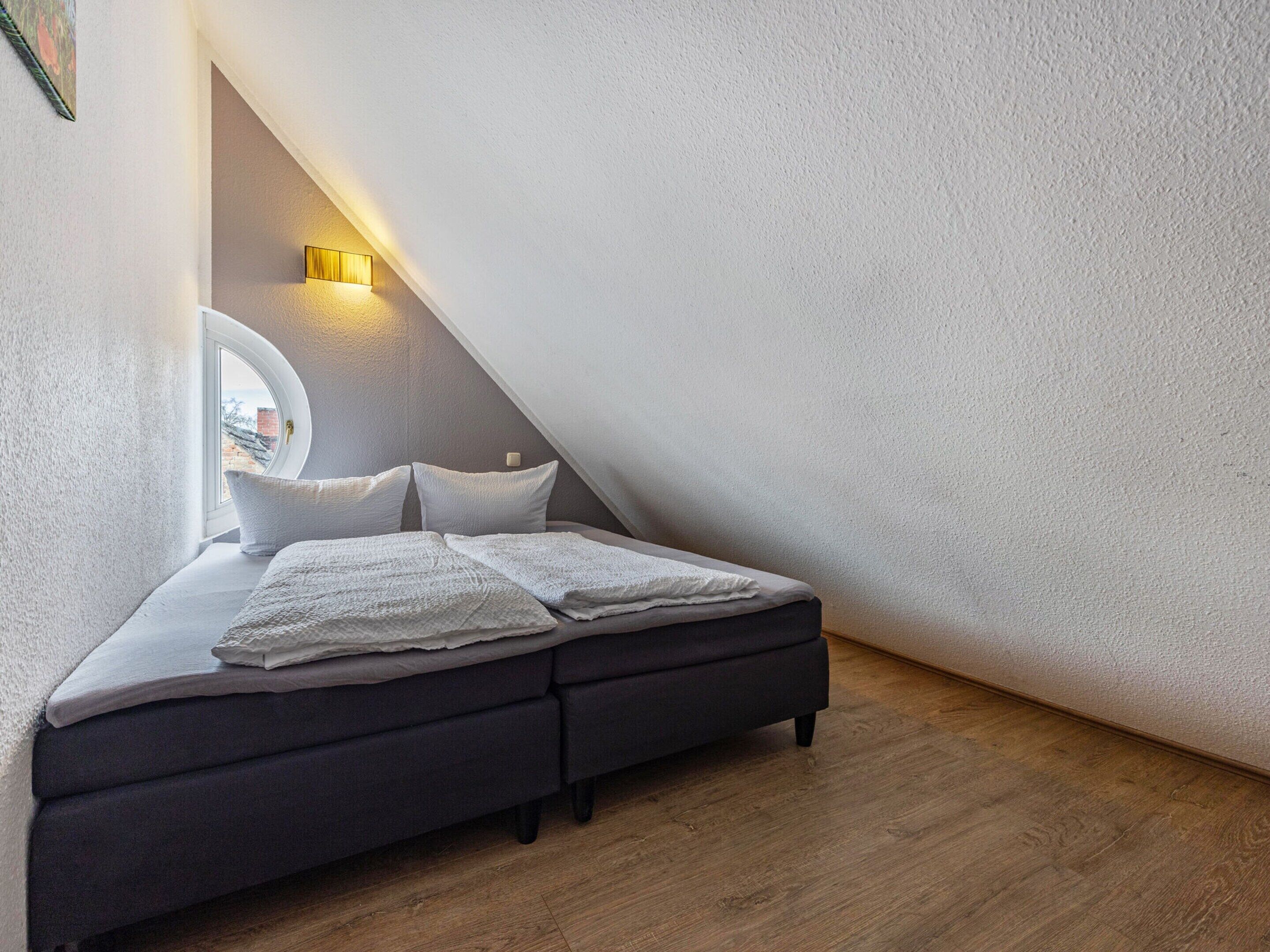 Un dormitorio con cama, almohadas, una lámpara de noche y vistas al exterior.