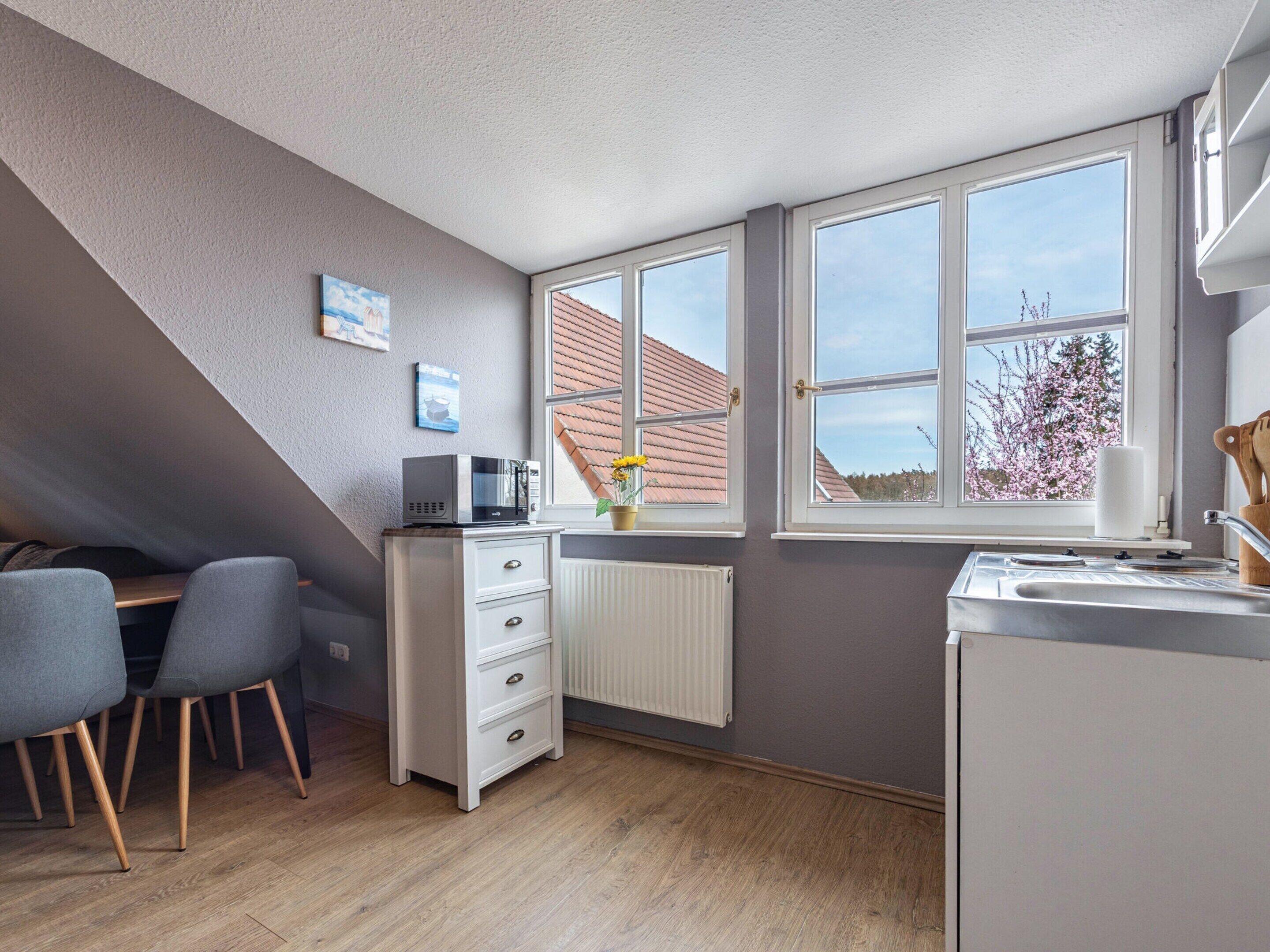A compact kitchen with a microwave, a sink, and a window overlooking a house.
