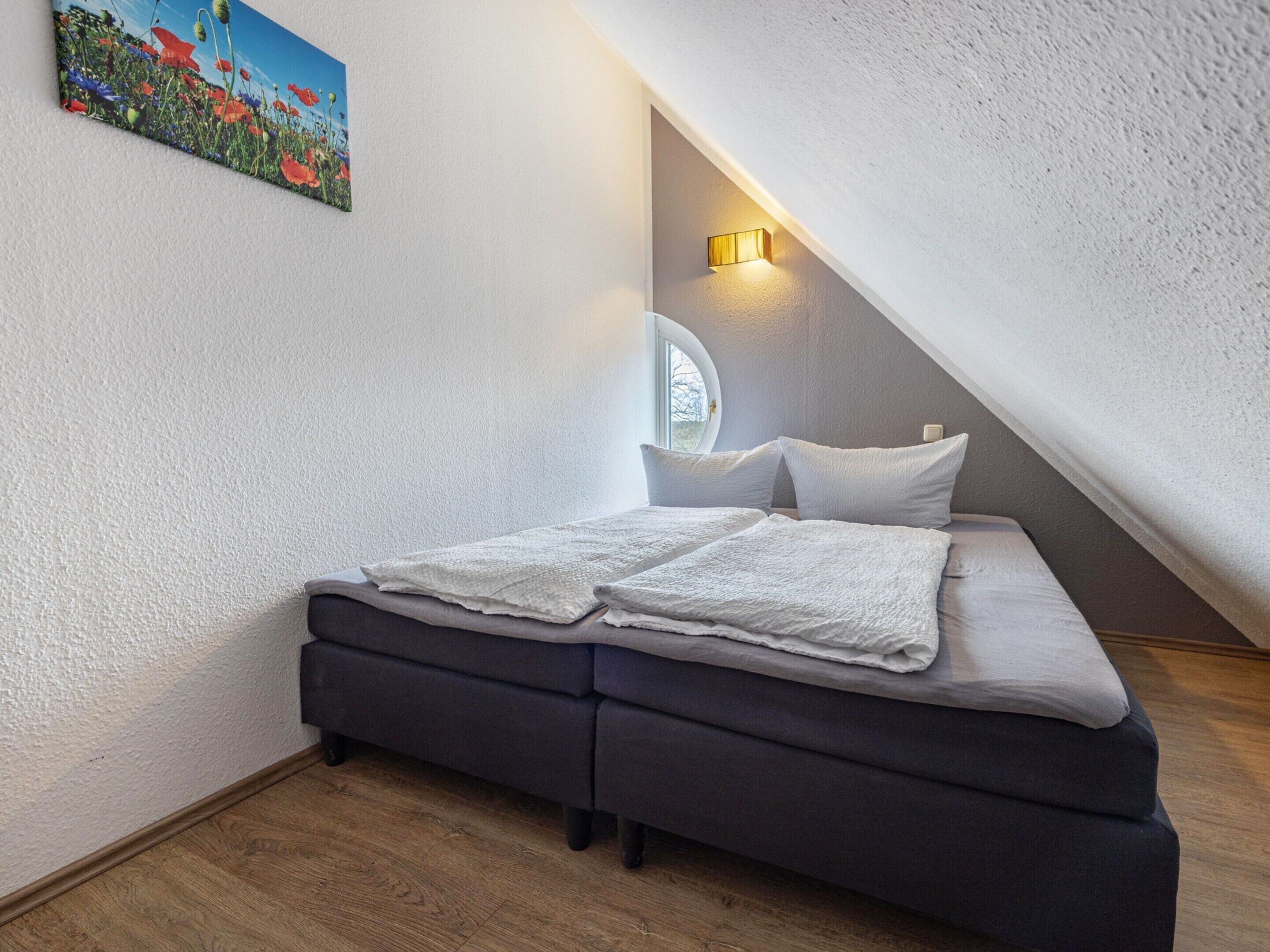 A bedroom with a bed, a window, and a painting on the wall.