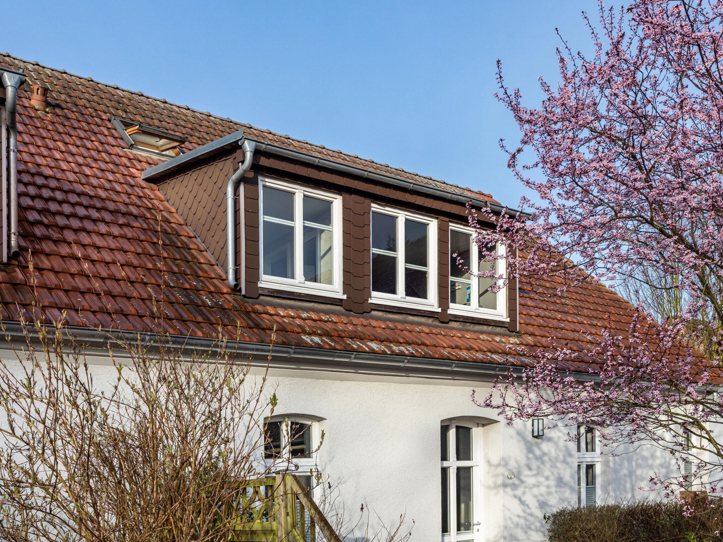 A two-story house with a brown tiled roof, white walls, and a dormer window.