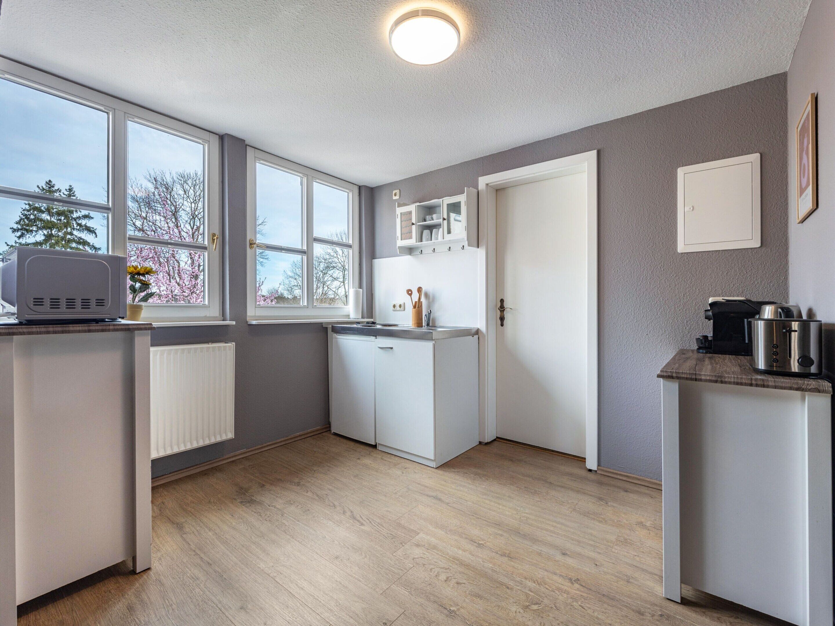 A compact kitchen with white cabinets, a built-in oven, and a window with a view of trees.