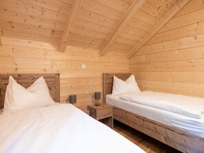 Eine Holzhütte mit zwei Etagenbetten, jeweils ausgestattet mit einem Kissen und einem Nachttisch mit Lampe.