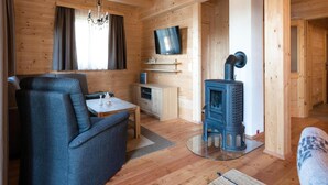 A cozy wooden cabin interior with a sofa, a dining table, a TV mounted on the wall, and a wood-burning stove. - Holiday Home in Stefan in the Lavanttal With Sauna (Frantschach-Sankt Gertraud)