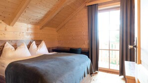 A wooden cabin bedroom with a bed, pillows, and a window with curtains. - Holiday Home in Stefan in the Lavanttal With Sauna (Frantschach-Sankt Gertraud)