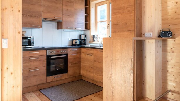 A modern kitchen with wooden cabinets, a built-in oven, a coffee maker, and a radio on a shelf. - Holiday Home in Stefan in the Lavanttal With Sauna (Frantschach-Sankt Gertraud)