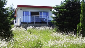 A modern building with a red roof and large windows, surrounded by a field of white flowers. - Ferienhaus Seeblick, Furstenwerder (Nordwestuckermark)
