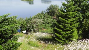 A lakeside view with dense greenery, a boat dock, and a grassy area with white flowers. - Ferienhaus Seeblick, Furstenwerder (Nordwestuckermark)