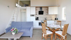 A compact living space with a sofa, dining table, and chairs, a kitchenette, and a staircase leading to an upper level. - Ferienhaus Seeblick, Furstenwerder (Nordwestuckermark)