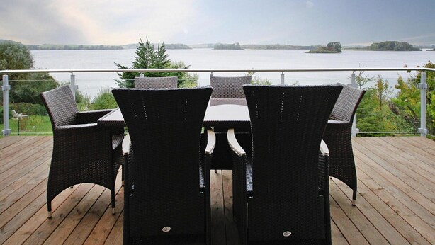 A deck with wicker chairs and a table overlooking a lake. - Ferienhaus Seeblick, Furstenwerder (Nordwestuckermark)