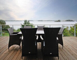 En træterrasse med fletstole og et bord med udsigt over en sø.