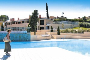 A swimming pool area with a person walking by, surrounded by a building with a stone facade and a clear blue sky.