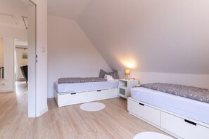 Ein modernes, gut beleuchtetes Zimmer mit zwei Betten, einem weißen Kleiderschrank und einem kleinen Nachttisch mit Lampe.