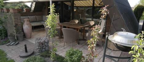 A patio with a dining table, chairs, a grill, and potted plants.