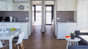 Une cuisine moderne avec des meubles blancs, un coin repas comprenant une table et des chaises, et un petit espace détente avec un canapé et une plante.