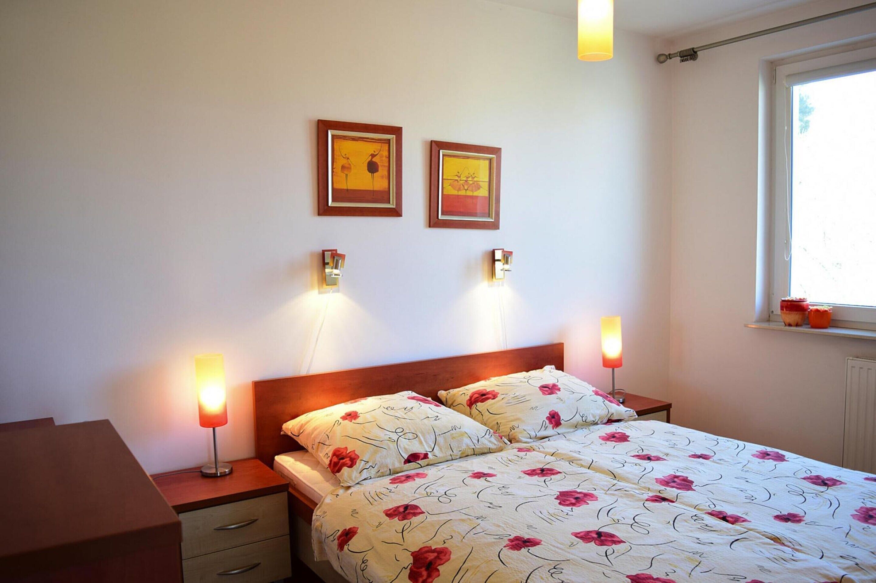 A bedroom with a bed, bedside lamps, a nightstand, a dresser, and two framed pictures on the wall.