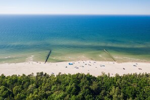 An aerial view of a beach with a sandy shore, clear blue water, and a forested area in the foreground. - Apartment in Ustka Near Baltic Sea Beach (Ustka)