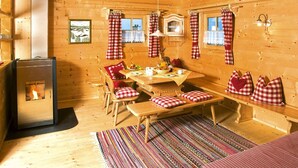 A cozy wooden cabin with a central wooden table, benches, and a fireplace.