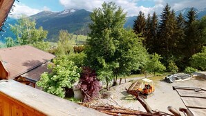 A wooden cabin with a view of a mountainous landscape, a dirt path, and construction equipment.