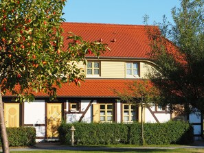 A traditional two-story house with a red-tiled roof, white walls with brown trim, and a small front garden. - Ferienwohnung im Feriendorf Rugana (Dranske)