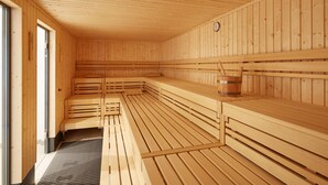 A sauna with wooden benches and a wooden wall with a clock. - Ferienwohnung im Feriendorf Rugana (Dranske)