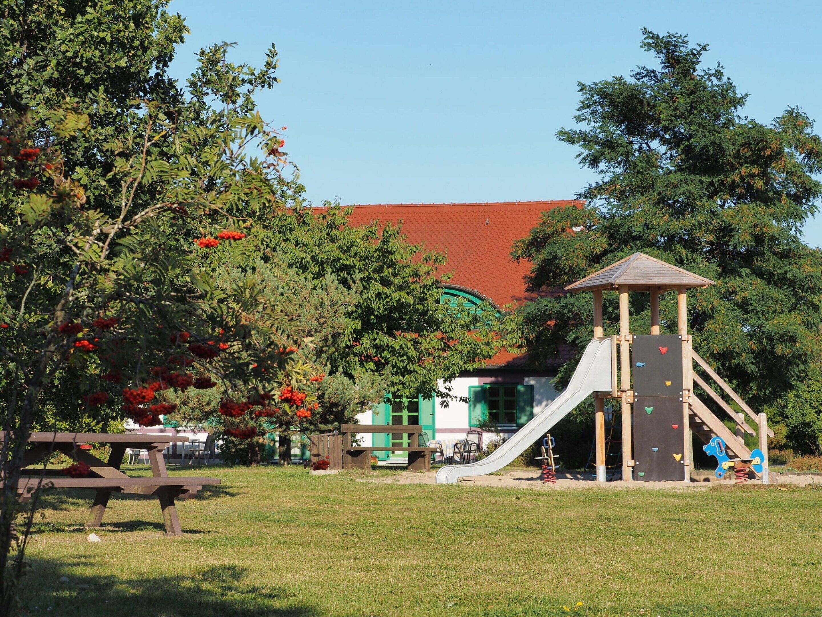 A playground with a slide and climbing wall, surrounded by trees and a picnic table.