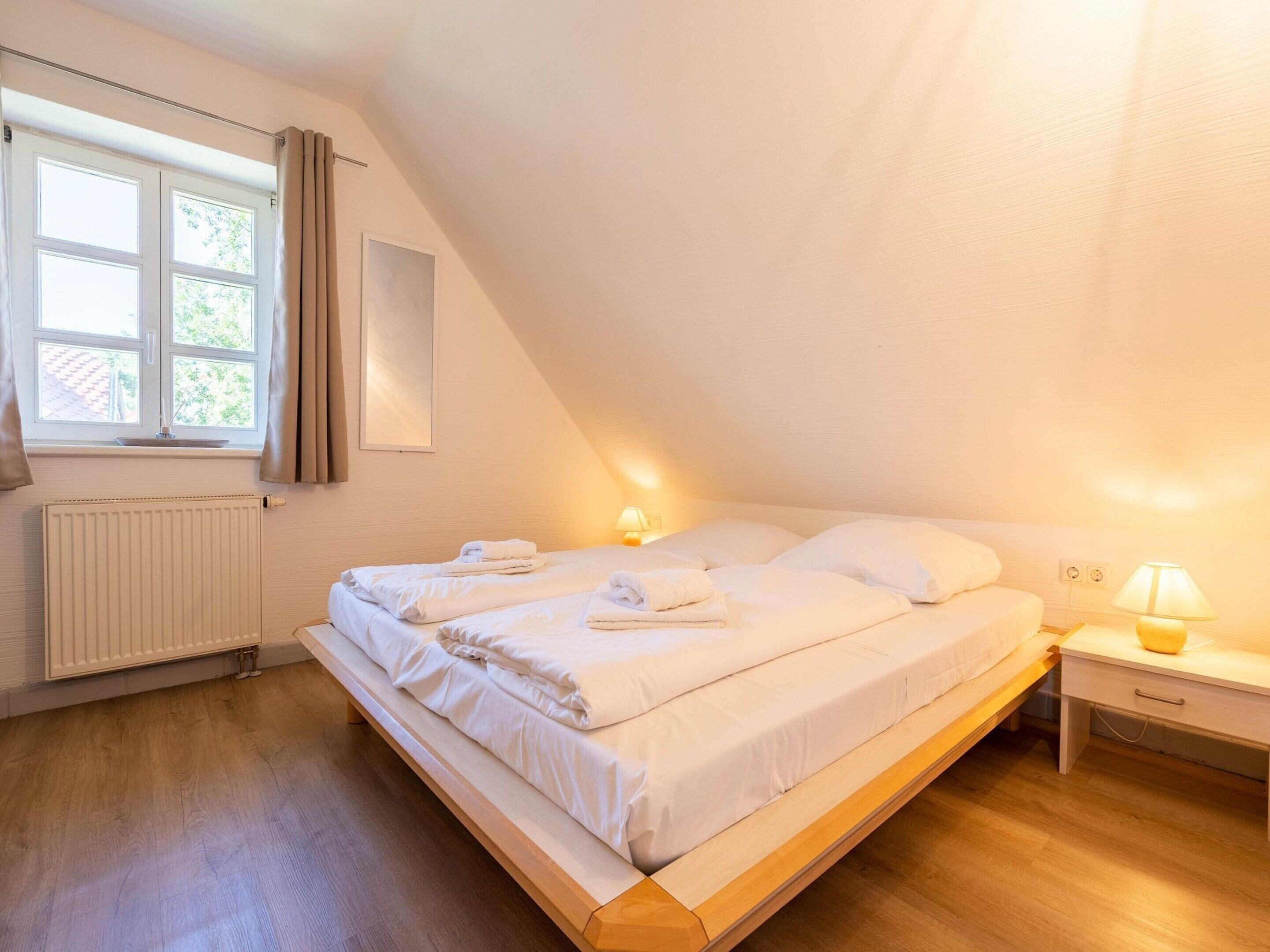 Una camera da letto con un letto grande, un comodino con una lampada, una finestra con tende e un termosifone.