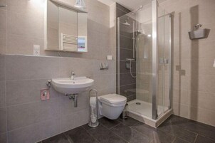 Egy modern fürőszoba mosdókagylóval, WC-vel és üvegfalas zuhanyzóval.