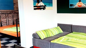 Ein Zimmer mit einem grauen Sofa, einem karierten Boden und einem Bett mit grün gestreiften Kissen.