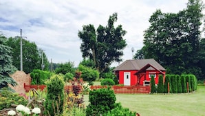 Ein rotes Haus mit einer weißen Tür, umgeben von einem gepflegten Garten mit verschiedenen Pflanzen und einem roten Zaun.