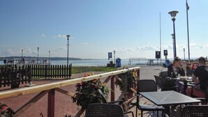 Ein Außenbereich mit Tischen und Stühlen, einer Holzterrasse und Blick auf das Meer.