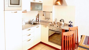A compact kitchen with white cabinets, a built-in microwave, a stove, and a sink. - 4-guest Porlezza Apartment Near Lake Lugano (Porlezza)