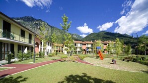 A hotel courtyard with a playground, a red running track, and mountain views. - 4-guest Porlezza Apartment Near Lake Lugano (Porlezza)