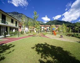 Un patio de hotel con un parque infantil, una pista de atletismo roja y vistas a la montaña.