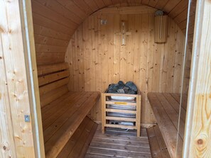Un sauna en bois, doté de bancs, et un banc en bois sur lequel repose un récipient en métal contenant des pierres.