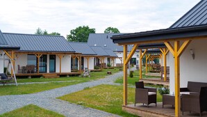 A row of cabins with outdoor seating areas, each with a covered porch and a gravel path between them. - Comfortable Cottages, Jezierzany (Postomino)