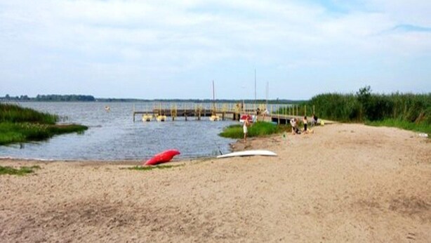 A beach with a pier extending into the water, a red kayak, and people in the distance. - Comfortable Cottages, Jezierzany (Postomino)