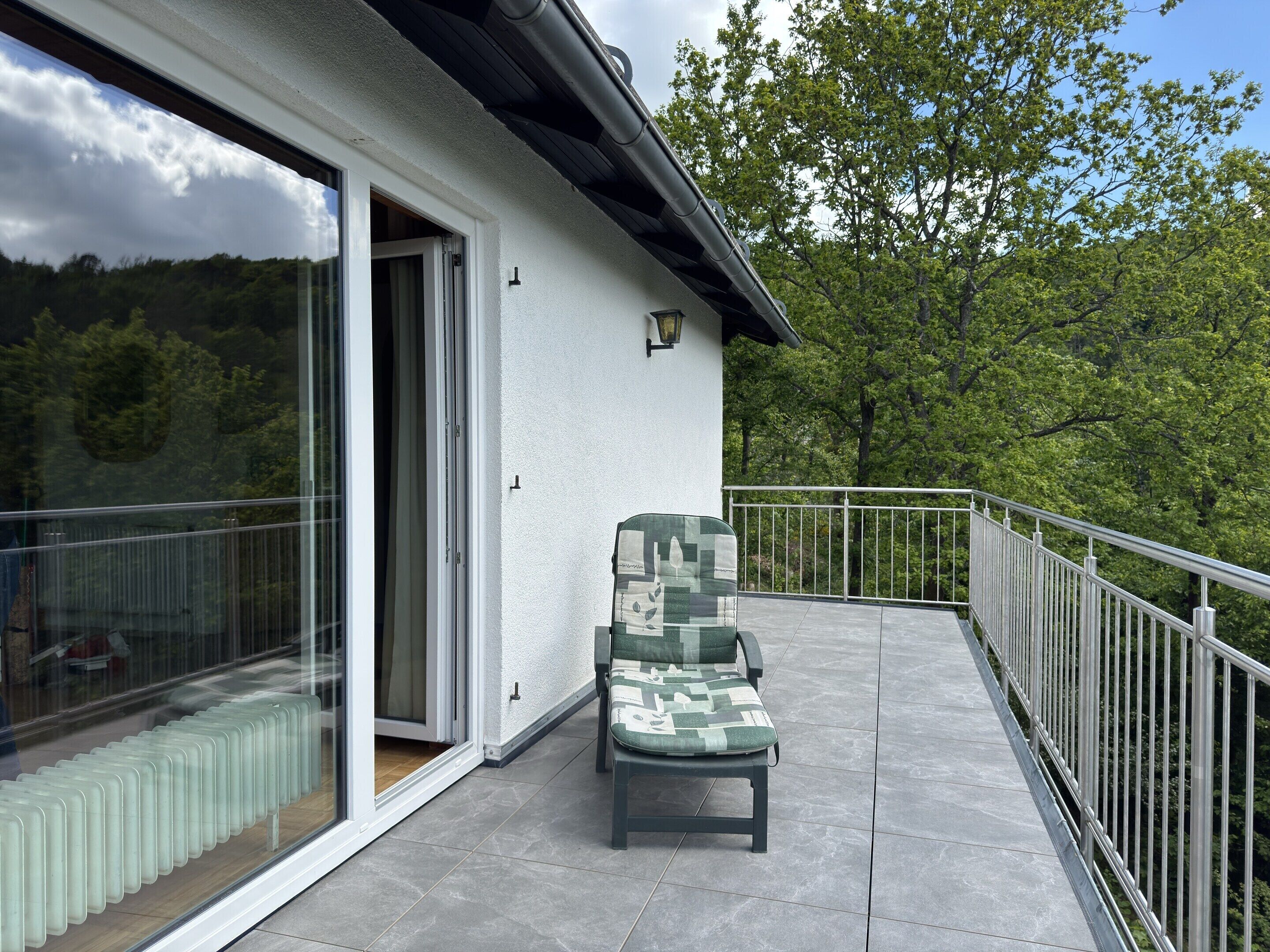 Ein Balkon mit gepolstertem Stuhl, einer Glastür und einem Metallgeländer.