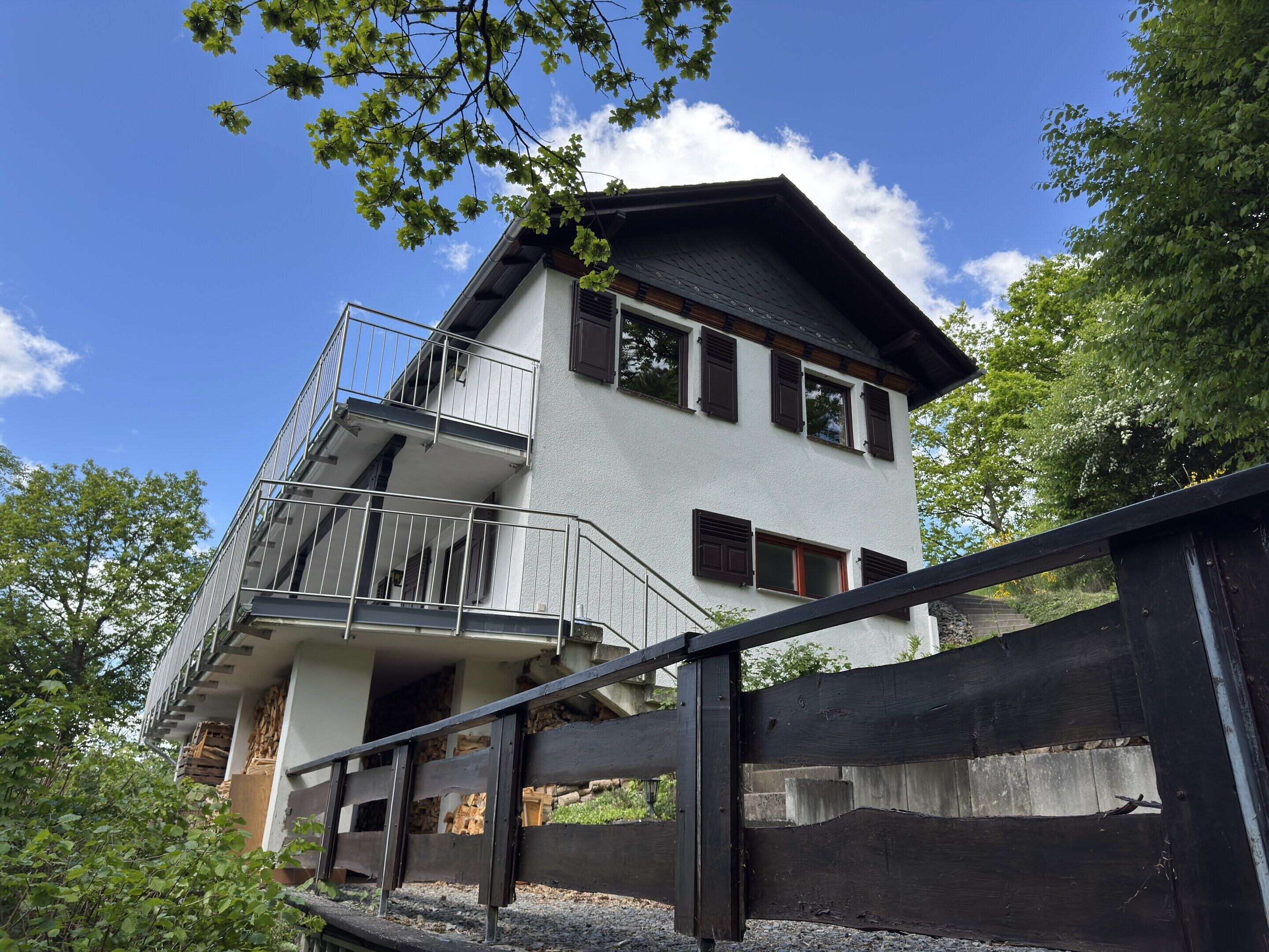 A two-story building with a balcony, a stone base, and a wooden fence.