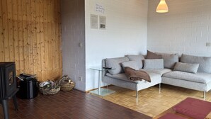 A modern living room with a grey sofa, a wooden floor, a glass table, and a hanging light fixture. - Ferienhaus Sackpfeifenblick, Hatzfeld (Hatzfeld)