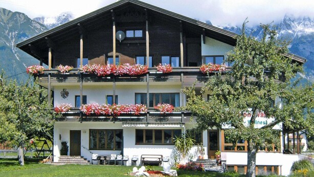 Un hôtel à plusieurs étages, doté de balcons ornés de fleurs, d’une entrée principale et surplombant un paysage montagneux.