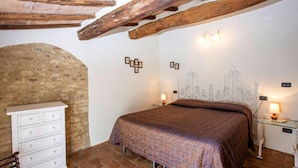 A bedroom with a bed, a dresser, and a stone wall. - Fattoria Bio Pieve a Salti, Montalcino (Montalcino)