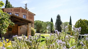 A brick building with a covered patio area, surrounded by a well-maintained garden with various plants and flowers. - Fattoria Bio Pieve a Salti, Montalcino (Montalcino)