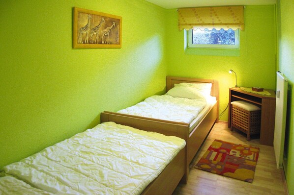 Una habitación pequeña con dos camas individuales, ventana con vistas, escritorio con lámpara y un cuadro de una jirafa en la pared.