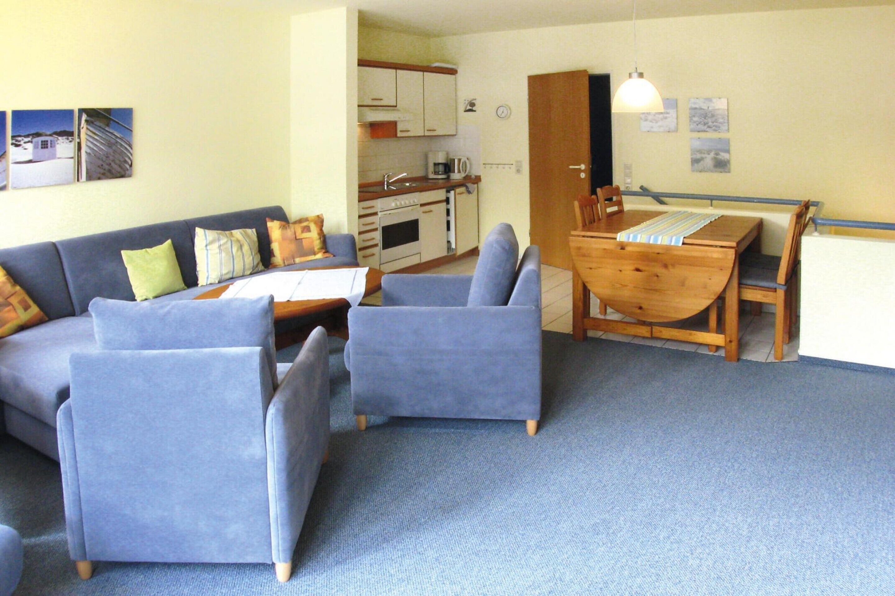 A compact living space with a sofa, two armchairs, a wooden dining table, and a kitchenette.