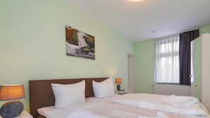 A hotel room with a bed, two bedside tables, a lamp, a painting, and a window with curtains. - Ferienwohnung Remise, Wernigerode (Wernigerode)