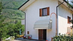 A white building with a sloped roof, wooden shutters, and a small porch with outdoor seating. - Holiday Home in Camaiore With Mountain Views (Camaiore)