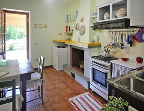 A compact kitchen with a stove, oven, and sink, a small refrigerator, and a dining area with a chair and table. - Holiday Home in Camaiore With Mountain Views (Camaiore)