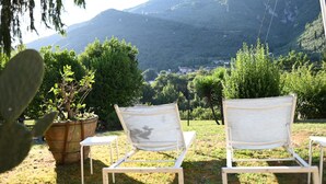 Two white lounge chairs facing a mountainous landscape with a view of a village in the distance. - Holiday Home in Camaiore With Mountain Views (Camaiore)